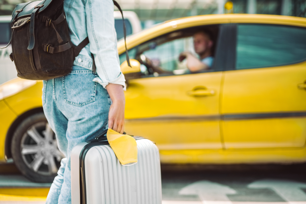Mulher aguardando táxi com máscara facial e mala de viagem